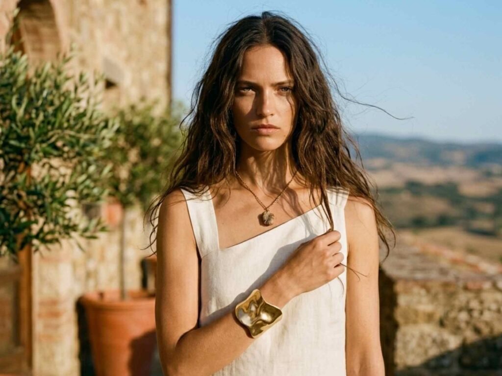 Una modella indossa un abito bianco in lino estivo con scollo asimmetrico, piega capelli naturale e morbida